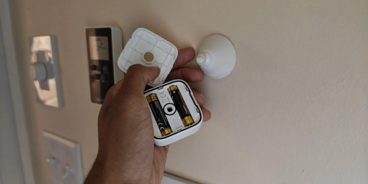 Hand holding a SwitchBot mmWave presence sensor with back cover removed and batteries visible