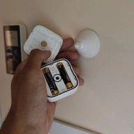 Hand holding a SwitchBot mmWave presence sensor with back cover removed and batteries visible